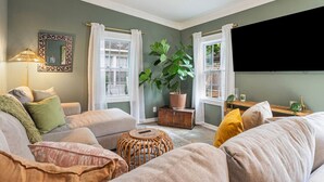 A living room with a sofa, a potted plant, and a television mounted on the wall. - Casa de Olas~3br/2ba Home with Backyard Oasis! (North Charleston)