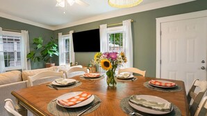 A dining room with a wooden table, chairs, a vase with flowers, and a ceiling fan. - Casa de Olas~3br/2ba Home with Backyard Oasis! (North Charleston)