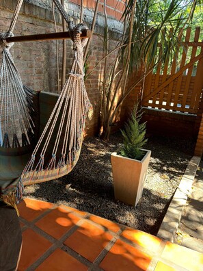 A hammock suspended between a brick wall and a wooden fence, with a potted plant and a tiled patio area. - Charming vintage chalet in the city—pets welcome! (Posadas)