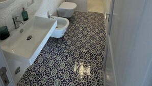 A bathroom with a white sink, a toilet, a bidet, and a shower area. - The Arcade on the sea. Charming view at 3 minutes walk from the beach (Santa Marina Salina)