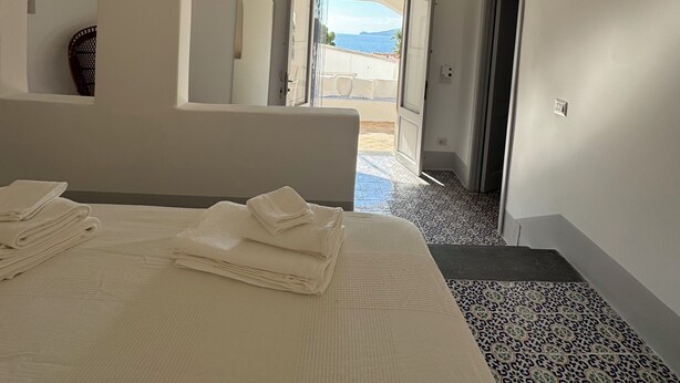 A bedroom with a bed, a ceiling fan, an open door leading to a balcony with a view of the sea. - The Arcade on the sea. Charming view at 3 minutes walk from the beach (Santa Marina Salina)