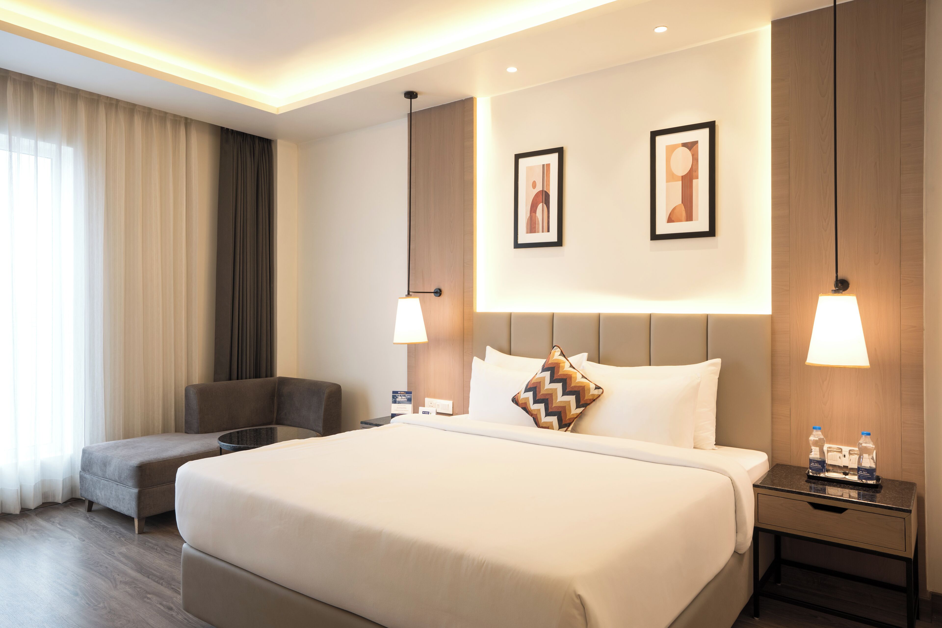 Una habitación de hotel con una cama grande, un escritorio, una silla y dos lámparas fijadas a la pared.