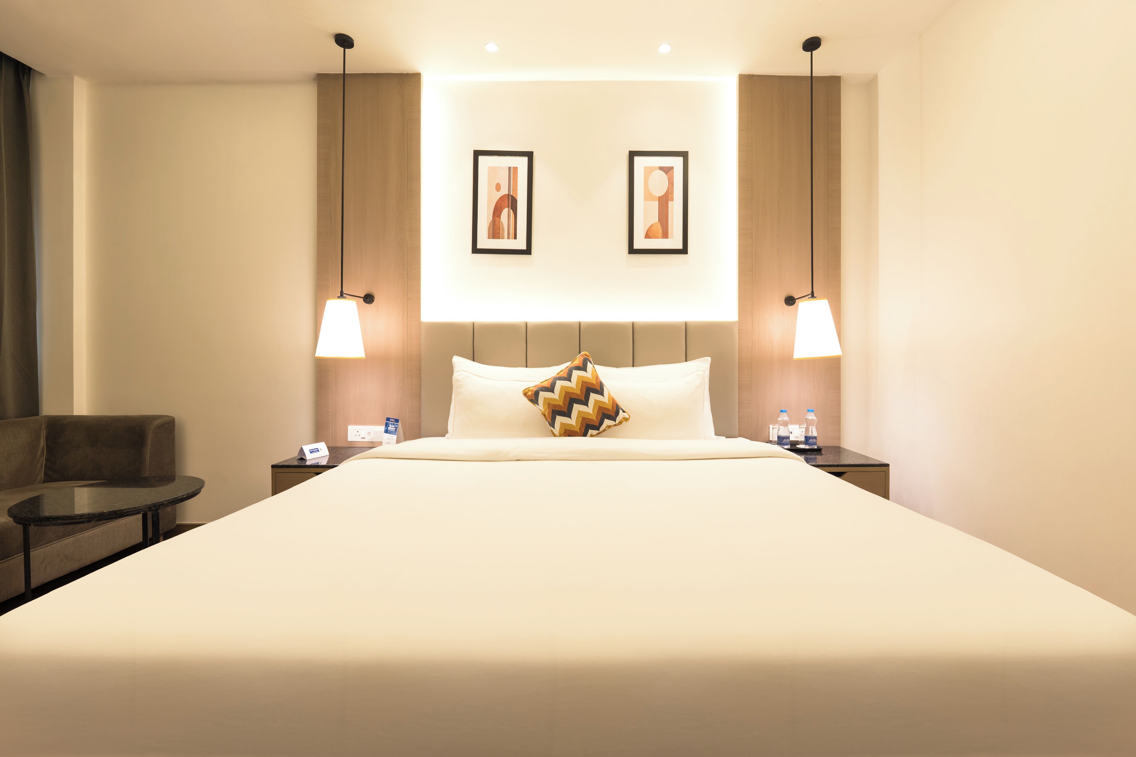 A hotel room with a large bed, two bedside tables, a chair, and two wall-mounted picture frames.