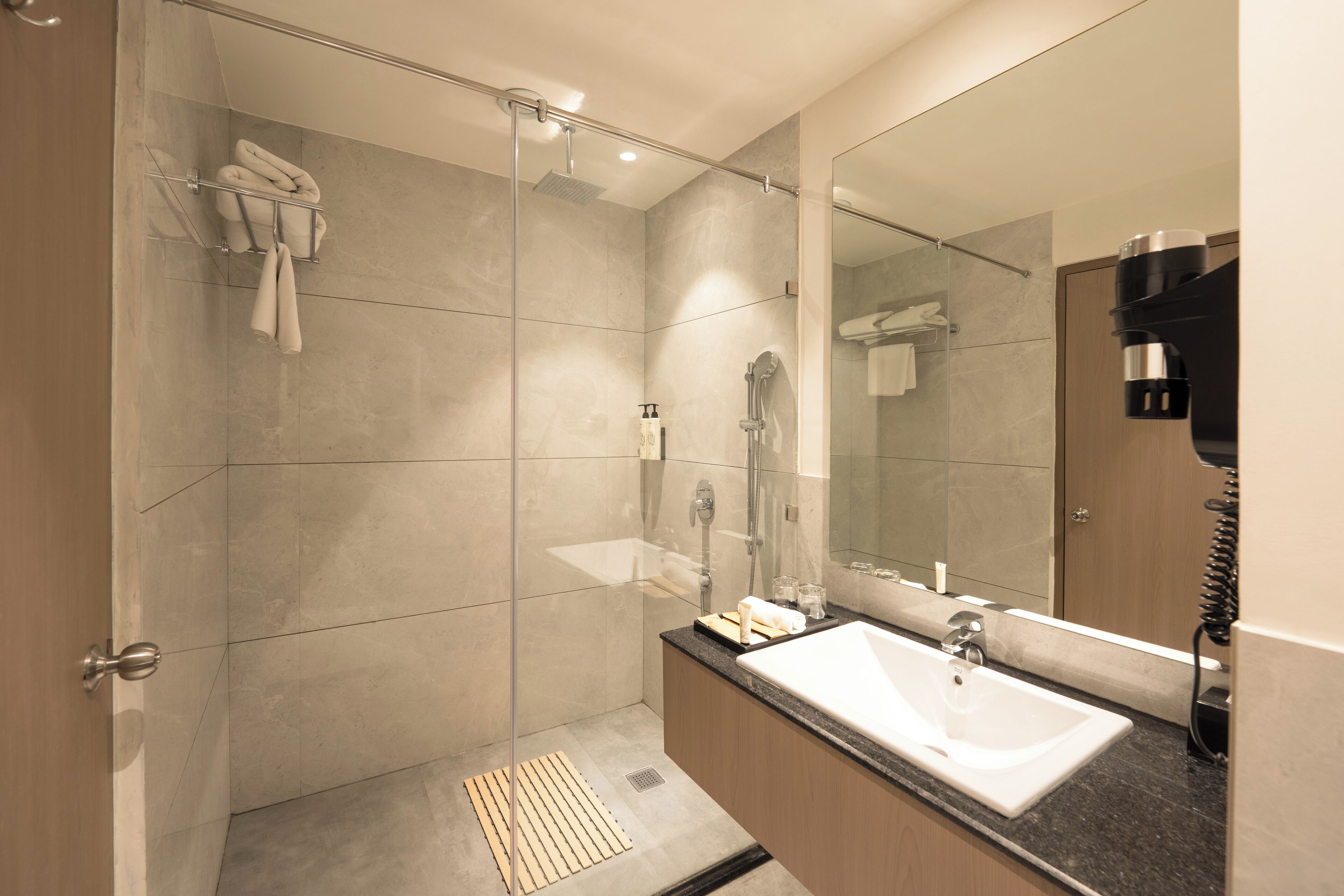 Un baño moderno con ducha de vidrio, un espejo grande y encimera de granito.