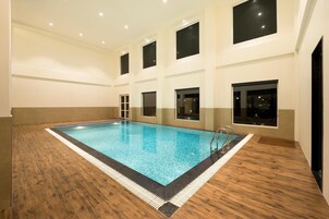 An indoor swimming pool with wooden flooring, multiple windows, and a tiled border.