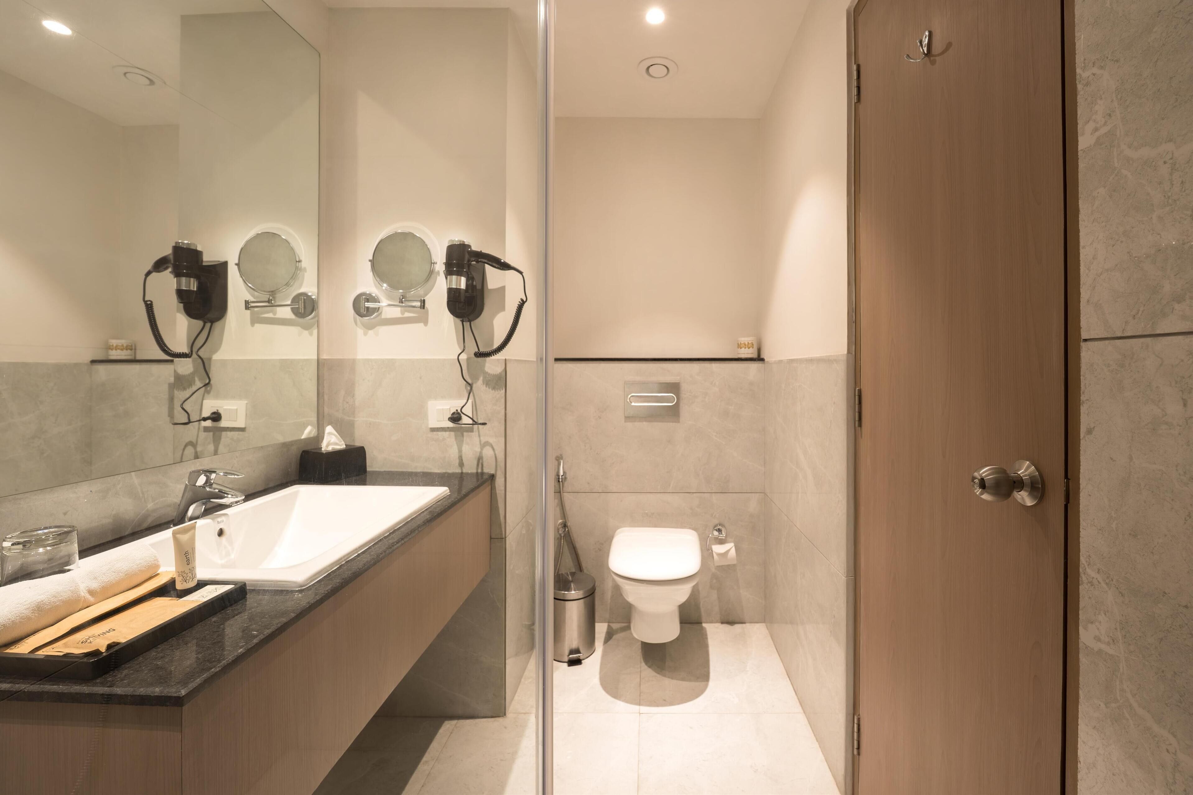 A modern bathroom with a large mirror, two hair dryers, a sink, and a toilet.