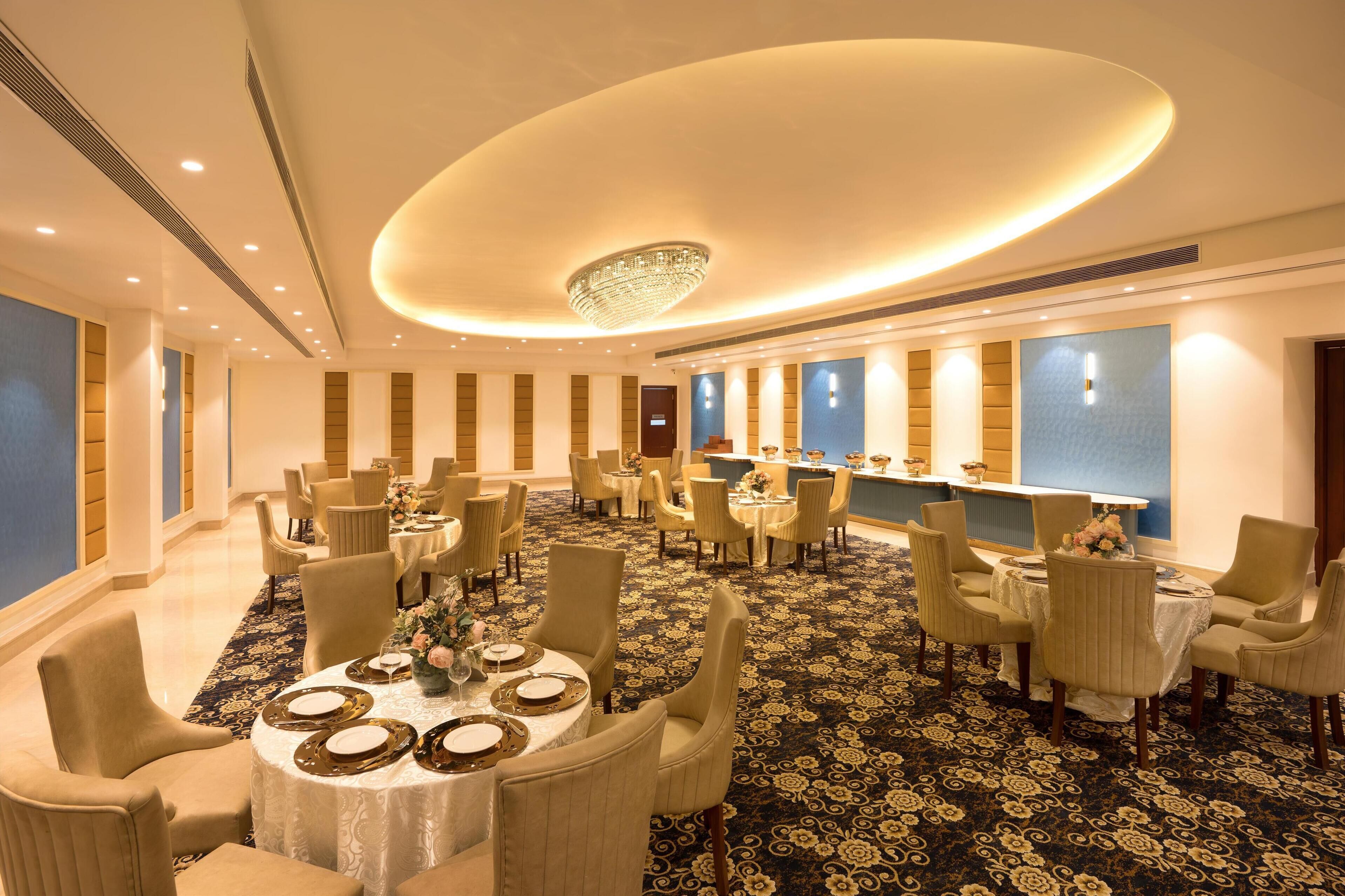 A hotel dining area with round tables, chairs, and a central chandelier.