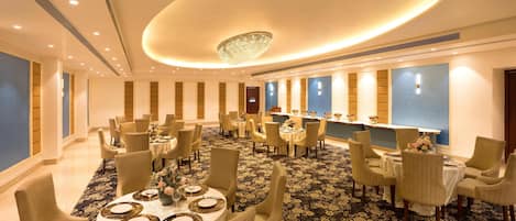 A hotel dining area with round tables, chairs, and a central chandelier.
