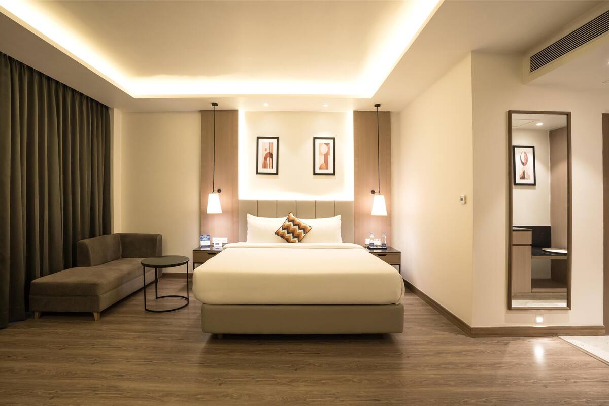 A modern hotel room with a large bed, a sofa, a small table, and two bedside lamps.