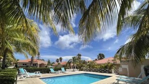 A rectangular pool with blue water, surrounded by palm trees and lounge chairs. - Serene & Centrally-located (Willemstad)