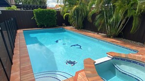 Una piscina rectangular con borde de azulejos, un jacuzzi y una terraza de madera alrededor.