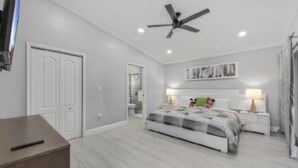 Un dormitorio con cama, mesitas de noche, ventilador de techo y televisión.