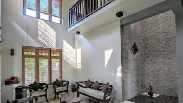 A spacious living area with a high ceiling, a balcony with a railing, and a stone accent wall.