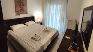 Una habitación de hotel con una cama grande, una mesita de noche con lámpara, un televisor y un cartel en la pared.
