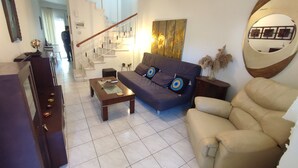 Una sala de estar con sofá, sillón, mesa de centro y una escalera que sube a un piso superior.