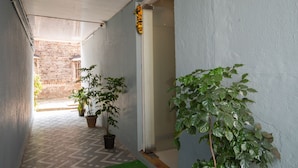 A narrow corridor with tiled flooring, potted plants, and a doorway leading to an outdoor area. - Hotel Stayland Inn (Mumbai)