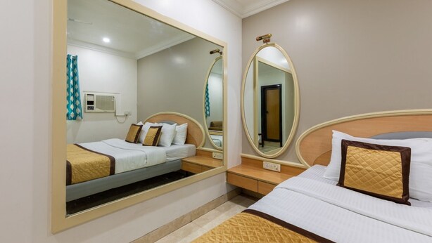 A hotel room with a bed, a nightstand, a mirror, and a wall-mounted air conditioning unit. - Hotel Stayland Inn (Mumbai)