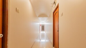 A hotel corridor with a wooden door on the right, a light switch on the left, and a hallway leading to another room. - Hotel Stayland Inn (Mumbai)