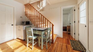 Una cocina con suelo de madera, una mesa de comedor con sillas, una escalera de madera y vistas a un baño.