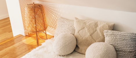 A cozy room with a white furry rug, a woven floor lamp, and several textured pillows.