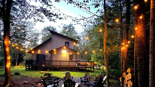 Een chalet met een terras, omringd door bomen en een zitgedeelte buiten.