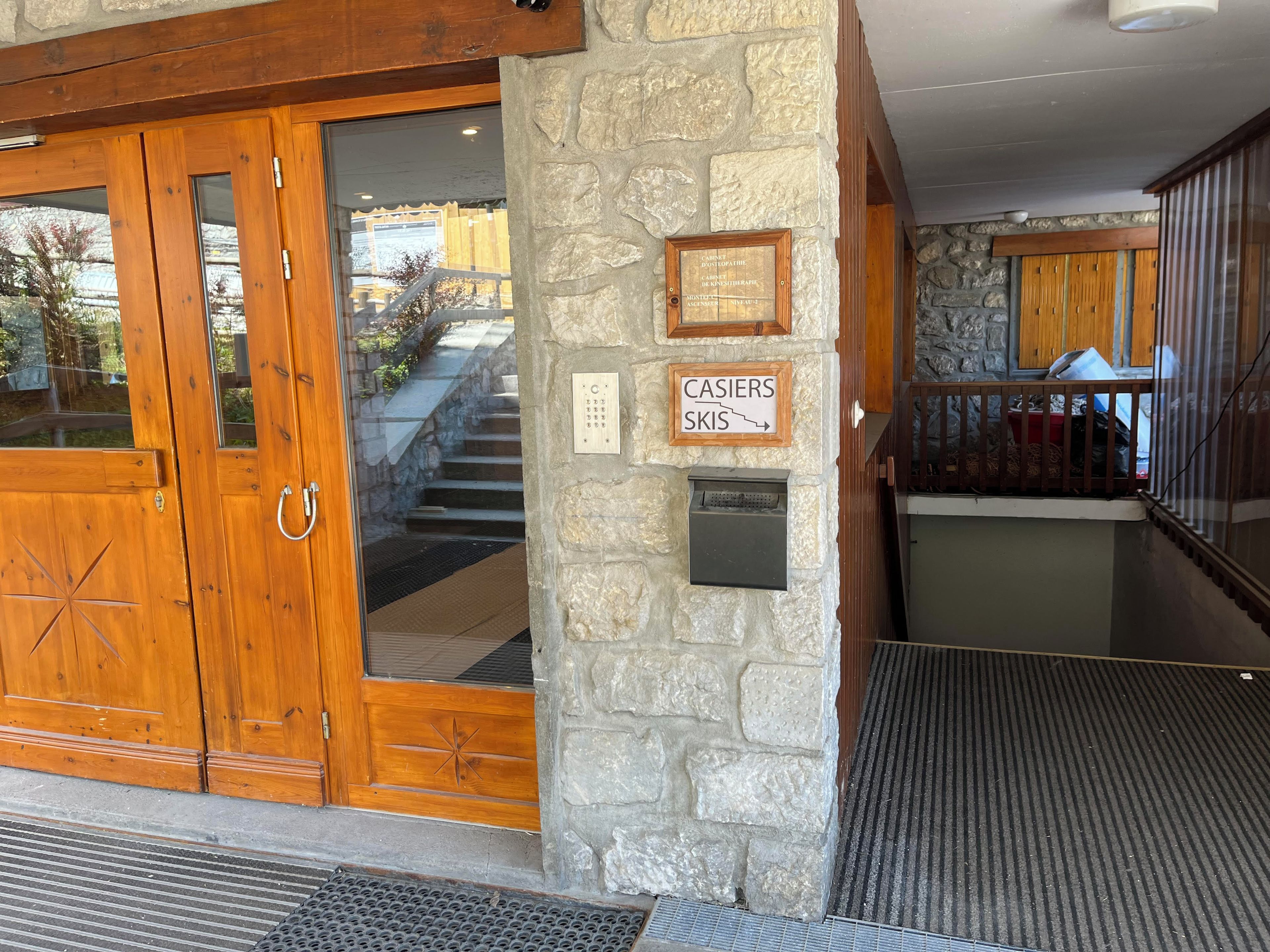 Une porte d’entrée en bois avec un panneau de verre, un mur en pierre orné d’une plaque et un panneau indiquant une zone de ski.