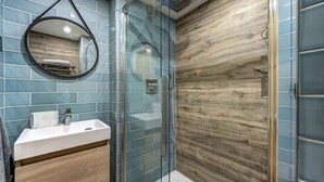 Un baño con cabina de ducha de vidrio, un lavabo blanco y una pared de madera.