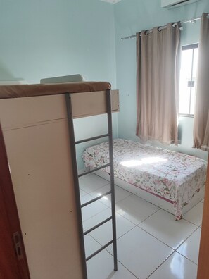A dormitory room with a bunk bed, a single bed with floral bedding, a window with curtains, and a tiled floor. - High-end house with swimming pool and 3 bedrooms (Plano Diretor Sul Palmas)