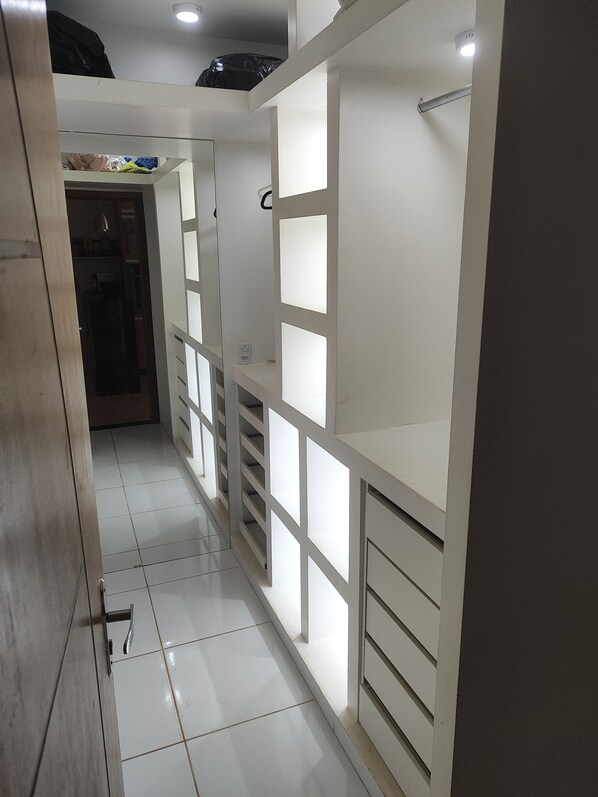 Un pasillo con piso de baldosas blancas, un marco de puerta de madera y un armario blanco con varios cajones y estantes.