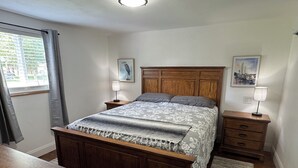 A bedroom with a wooden bed, two bedside tables with lamps, a wooden dresser, and a window with curtains.