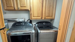 A compact laundry room with two stainless steel washers and dryers, wooden cabinets above, and a visible power outlet.