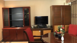 A room with a dining table, red chairs, a television on a stand, and a cabinet with glass doors. - Sea Shell Hotel & Restaurant (Dhaka)
