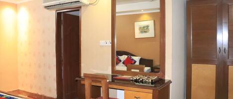 A bedroom with a bed, a wooden desk with a chair, a wardrobe, and a mirror.