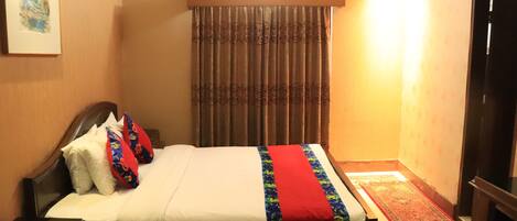 A neatly made bed with a red and blue bedspread, a wooden headboard, and a nightstand with a lamp.