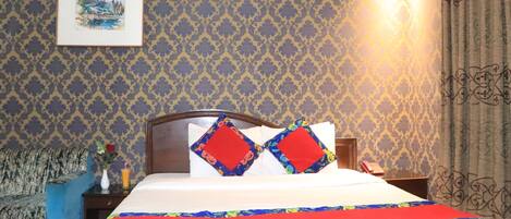 A hotel room with a bed, a nightstand, a lamp, a framed picture on the wall, and a patterned wallpaper.