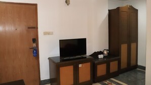 A hotel room with a wooden wardrobe, a television on a cabinet, and a coffee maker on the side table. - Sea Shell Hotel & Restaurant (Dhaka)