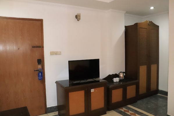 A hotel room with a wooden wardrobe, a television on a cabinet, and a coffee maker on the side table. - Sea Shell Hotel & Restaurant (Dhaka)