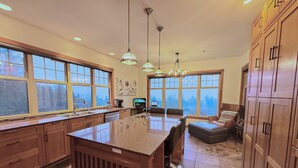 A spacious kitchen with a large island, wooden cabinets, and multiple windows offering views of the outdoors.