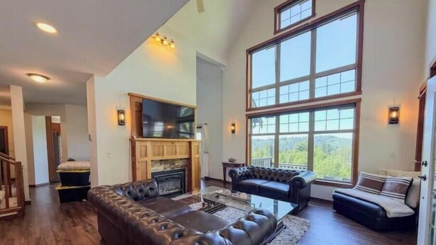 A spacious living room with a large sectional sofa, a fireplace, and a large window offering a view of the outdoors.