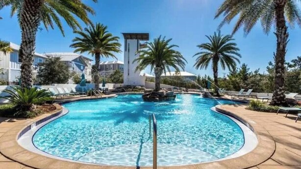 Una piscina con palme e lettini prendisole tutt'intorno.