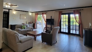 A spacious living room with a sofa, armchairs, a coffee table, and a TV. There is a sliding glass door leading to an outdoor area. - Rosita with a Waterfall Jacuzzi & Rain Forest feel (Lambeau)