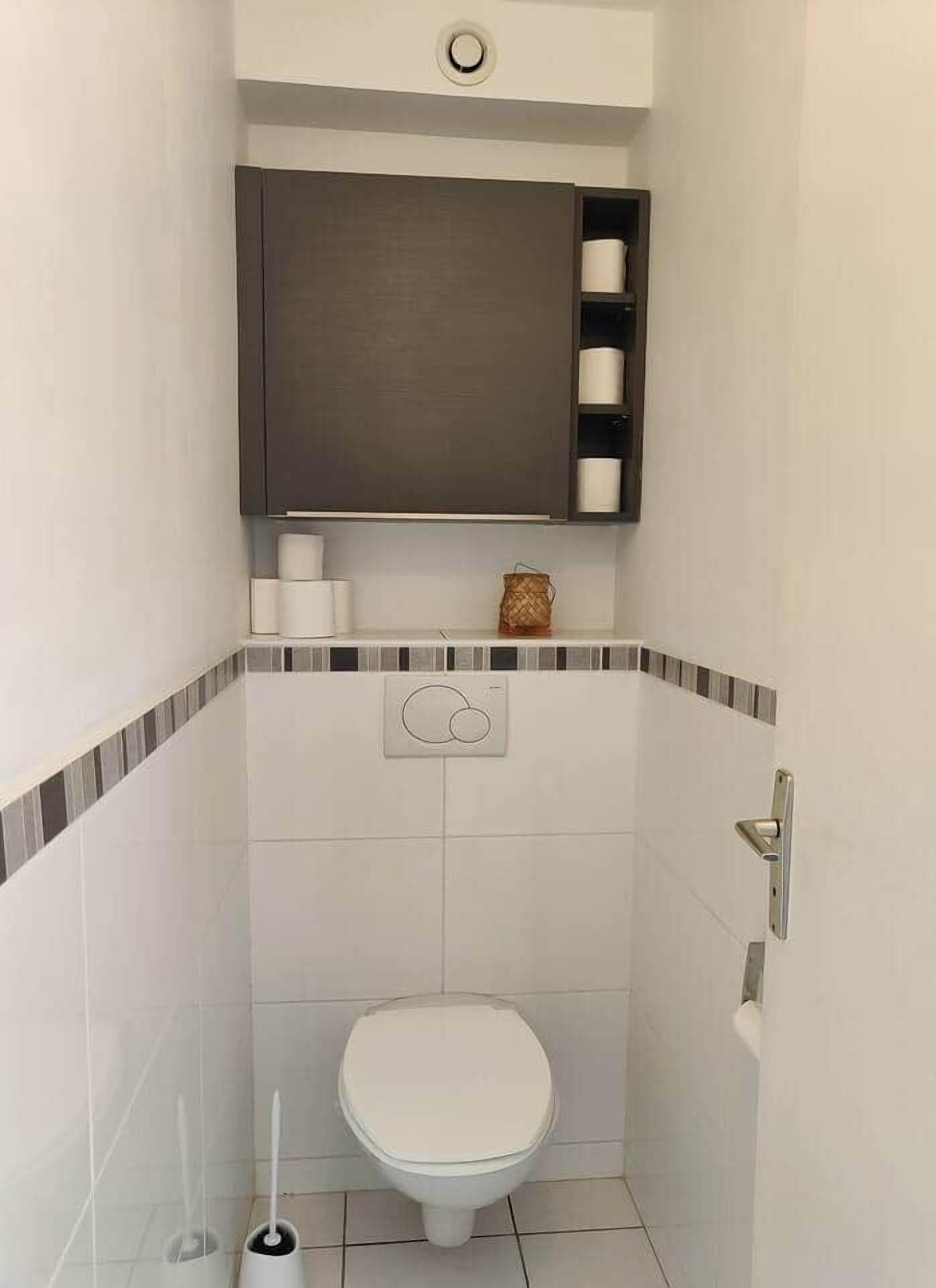 Ein kleines, kompaktes Badezimmer mit Toilette, Handtuchhalter und einem Schrank über der Toilette.