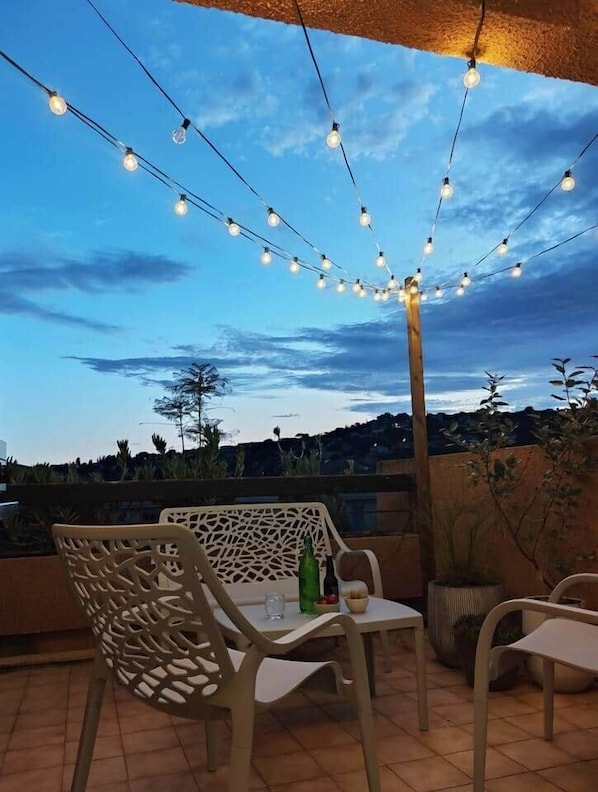 An outdoor patio with string lights, a table with chairs, and a view of the sky and landscape.
