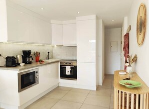 A modern kitchen with white cabinets, a built-in oven, a microwave, and a coffee maker.