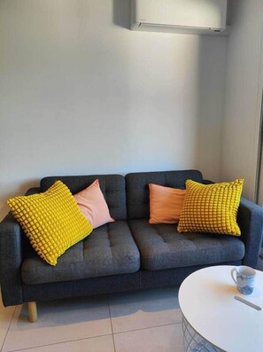 A modern living room with a dark grey sofa, two yellow textured pillows, and a white coffee table with a cup.