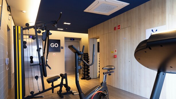 Ein Fitnessraum mit Trainingsgeräten, einem Laufband und einem an der Wand befestigten Schild mit der Aufschrift 'GO'.