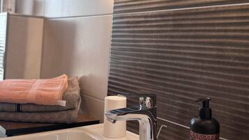 A modern bathroom with a large mirror, a white sink, a chrome faucet, and a bottle of shampoo.