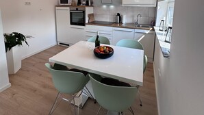A modern kitchen with white cabinets, a dining table with chairs, and a fruit bowl on the table. - Dariana Schwalbach/Saar (Schwalbach)