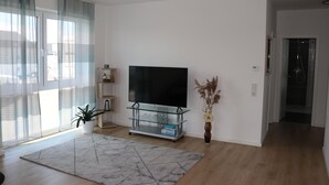 A modern living room with a flat-screen TV on a glass TV stand, a potted plant, and a vase with dried flowers. - Dariana Schwalbach/Saar (Schwalbach)
