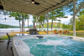 A hot tub area with a view of a lake, surrounded by trees and outdoor furniture.